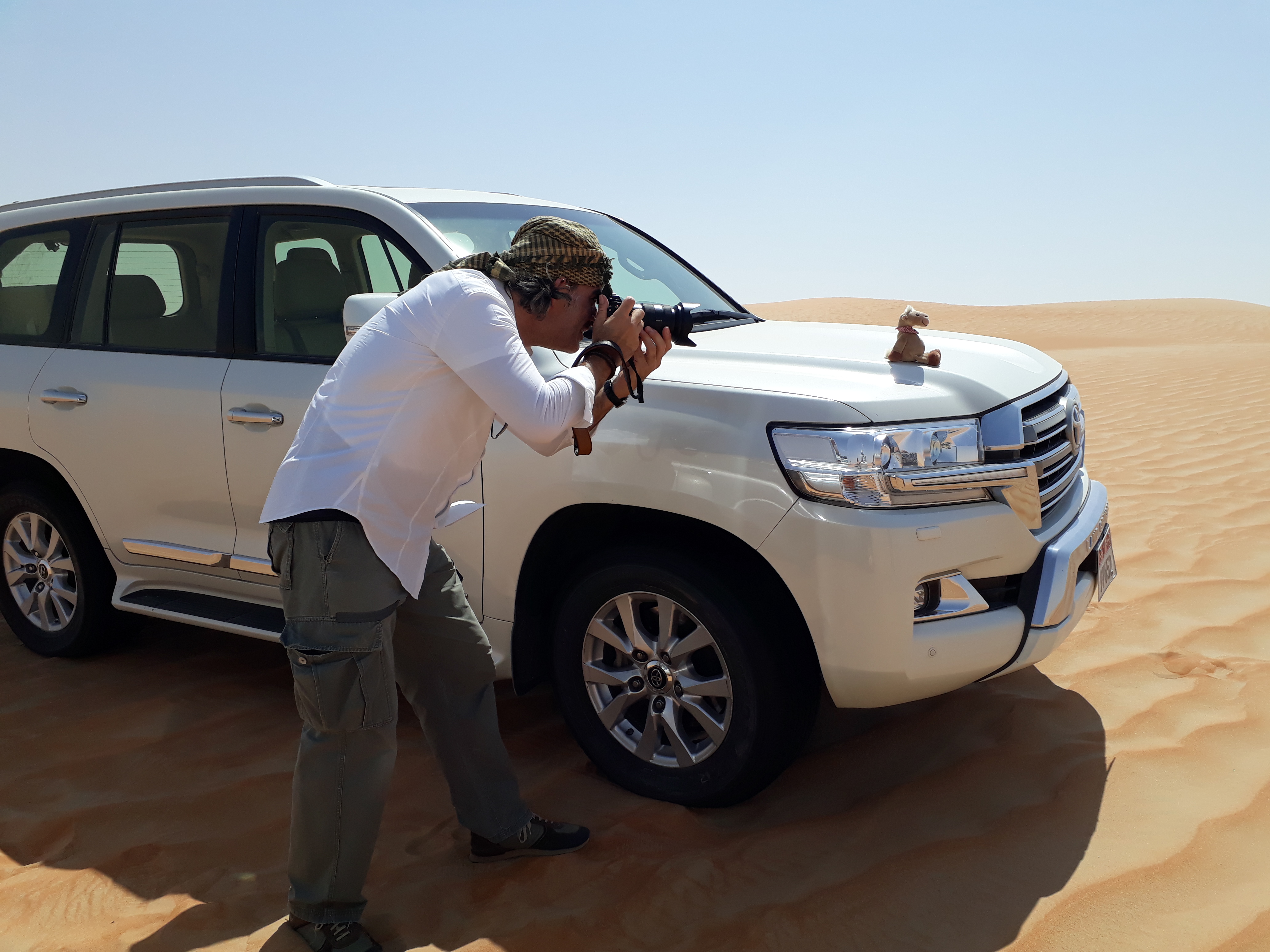 A photographer takes a picture of a toy camel on the bonnet of a Nissan Patrol while in the desert