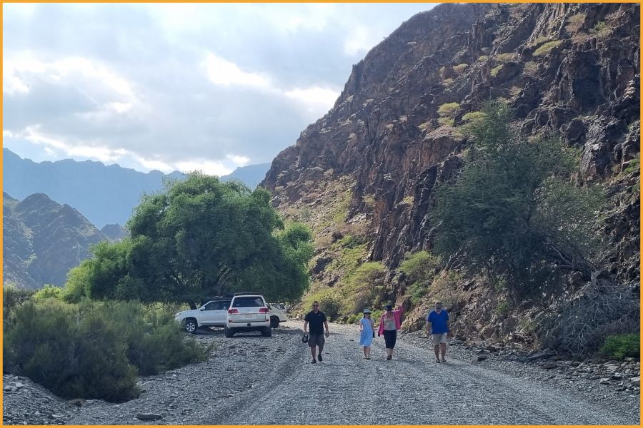 Small group of travellers walking along a mountain track in Wadi Sahtan, Oman, surrounded by rugged cliffs and greenery, showing the region’s calm outdoor adventure appeal