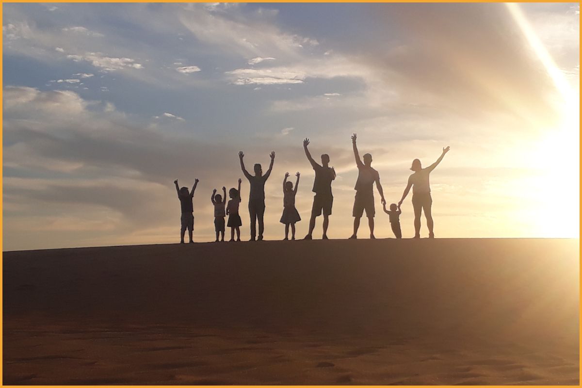 Parents and children silhouetted on a desert dune at sunset in the Arabian Peninsula, evoking a safe, joyful family travel experience