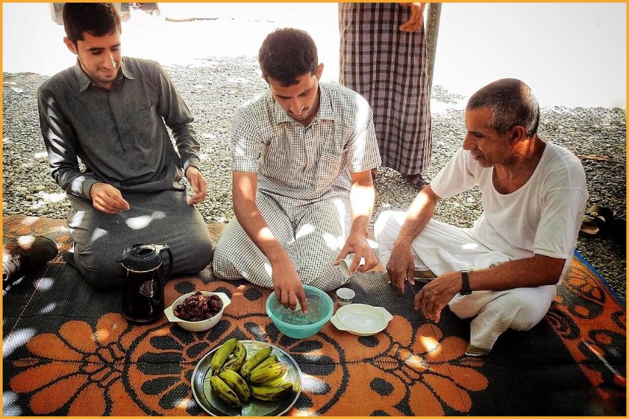 Omani hosts welcoming travellers into a date-palm garden, sharing qawa coffee, dates and fruit — a moment of everyday hospitality on the Arabian Peninsula